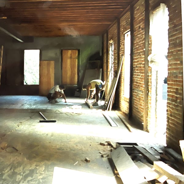 Two workers renovating the Cafe Santorini interior, with exposed brick walls and wooden ceilings.