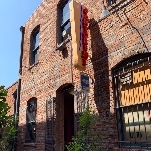 The Cafe Santorini sign hangs on a brick building with arched windows and metal grates.