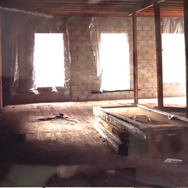 Unfinished restaurant interior with exposed brick walls, wooden beams, and bright windows covered in plastic.
